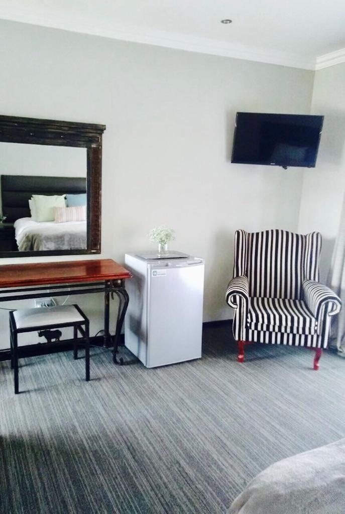 A hotel room with a desk, a small refrigerator, a striped armchair, and a television mounted on the wall.