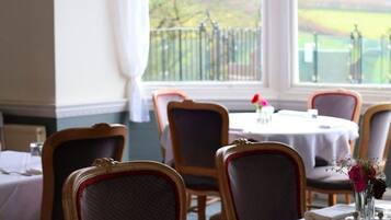 Comedor con mesa lista para dos personas, sillas y vista a un campo cercado a través de amplios ventanales.