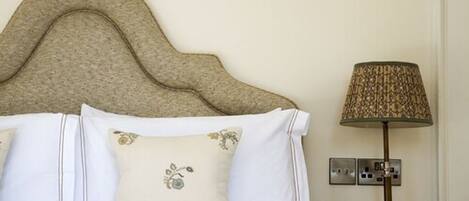 A neatly made bed with white linens and decorative pillows, a textured headboard, and a lamp on a bedside table.