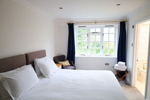 Habitación de hotel con una cama grande, una silla, un ventanal con cortinas y vistas al exterior.