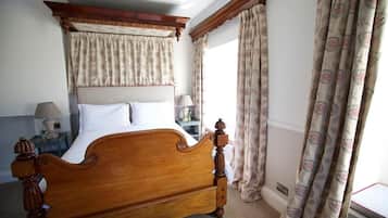 Un dormitorio con una cama baldaúquina de madera, una mesita de noche con lámpara y cortinas estampadas.