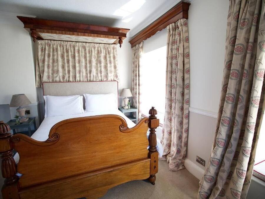 A bedroom with a wooden four-poster bed, a nightstand with a lamp, and patterned curtains.