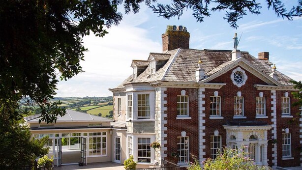 A large, historic building with a prominent clock tower, a conservatory, and a well-maintained garden. - The Eagle House Hotel (Launceston)