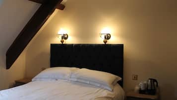 Una cama bien hecha con sábanas blancas, cabecera oscura y dos lámparas de pared.