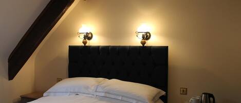 Una cama bien hecha con sábanas blancas, cabecera oscura y dos lámparas de pared.