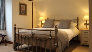 A bedroom with a four-poster bed, two bedside tables with lamps, a nightstand, a framed picture on the wall, and a window with curtains. - The Eagle House Hotel (Launceston)