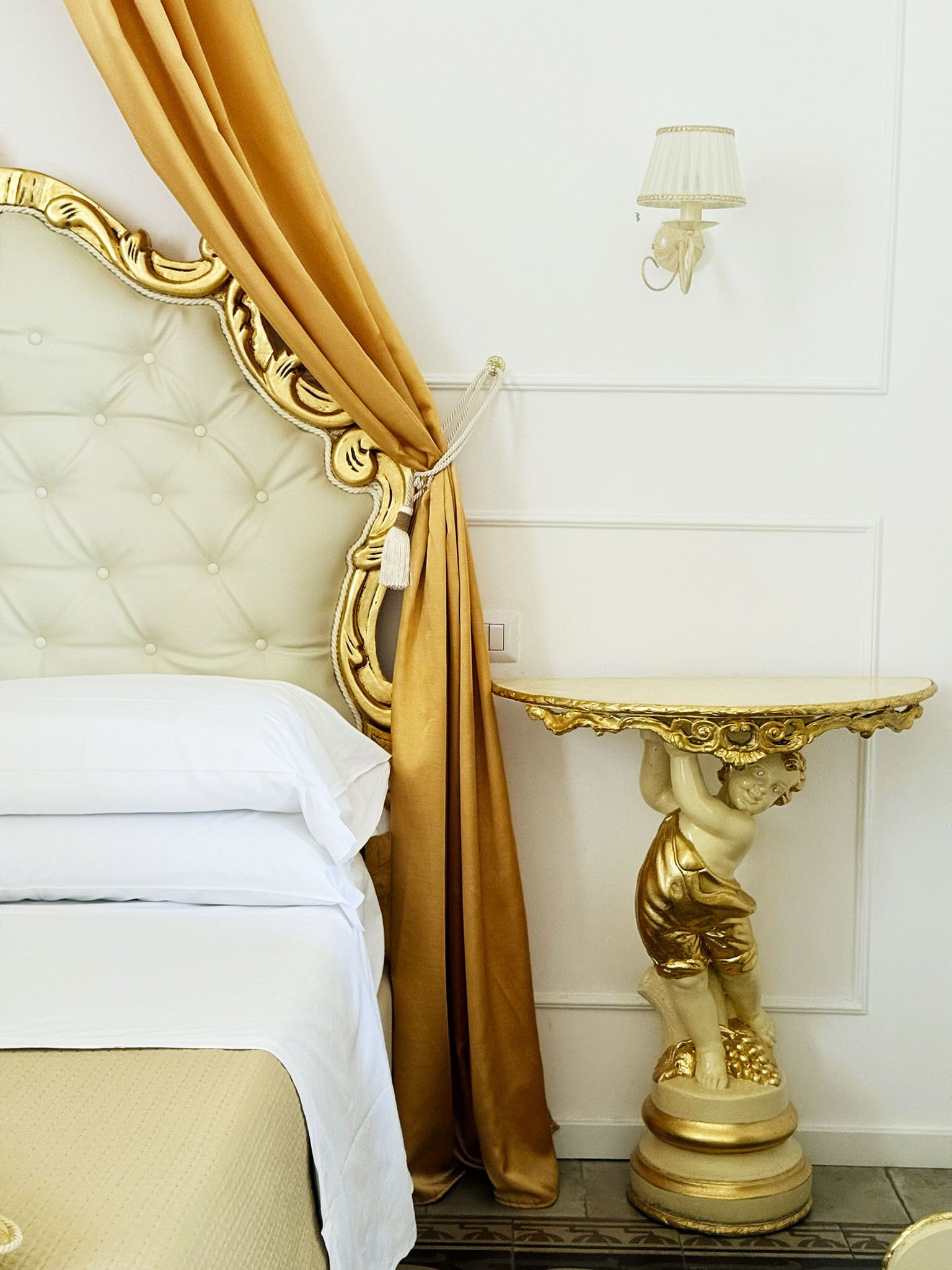 Ein Bett mit weißen Leinen, einem goldfarbenen Vorhang und einer goldenen Statue auf einem Sockel.