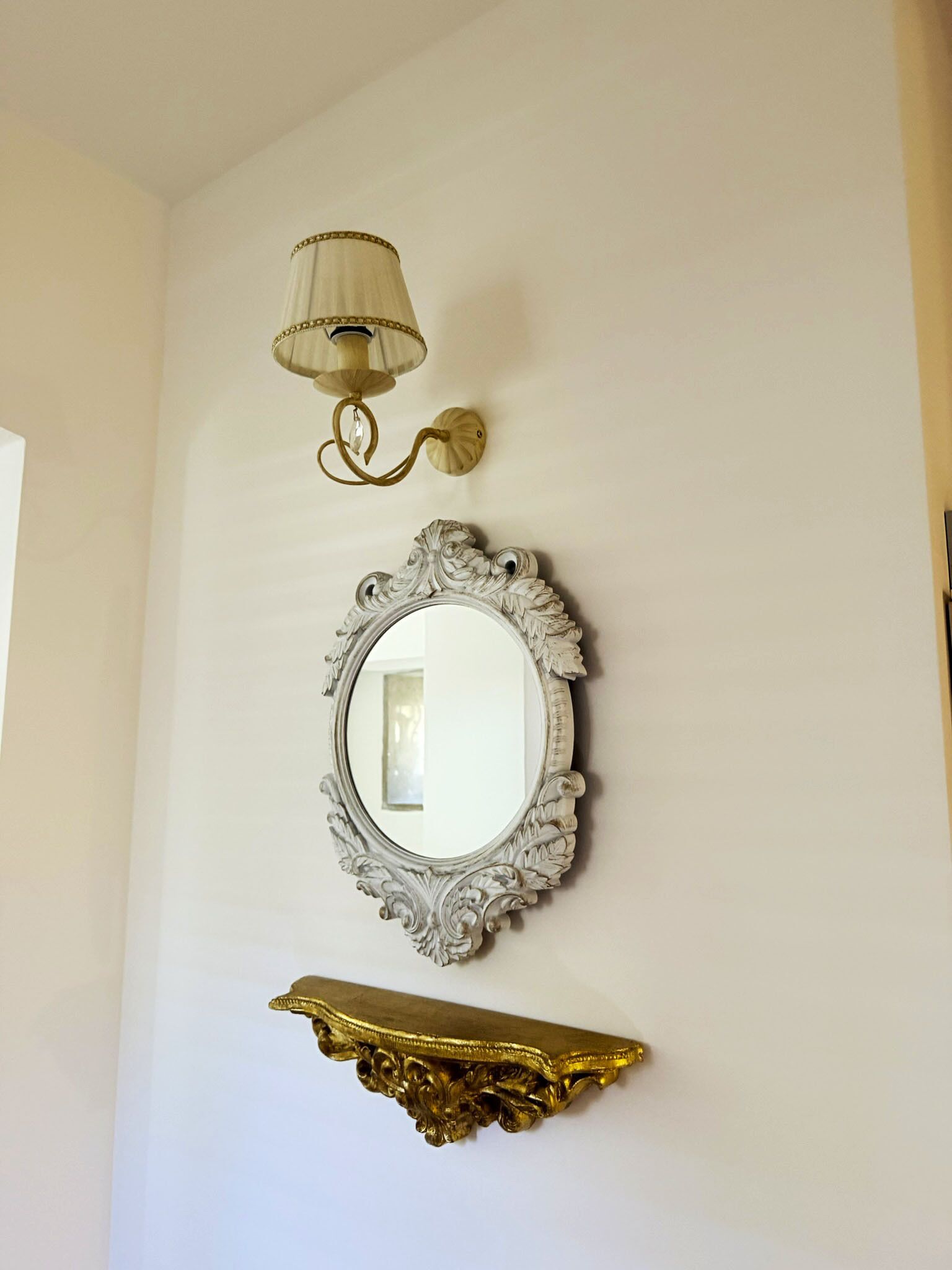 Un miroir mural avec un cadre orné, une applique murale et une étagère décorative dorée.