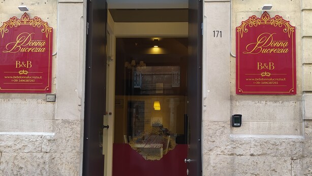 Entrada de un hotel con un letrero rojo que dice 'Donna Bucrezia B&B' y un número de teléfono.