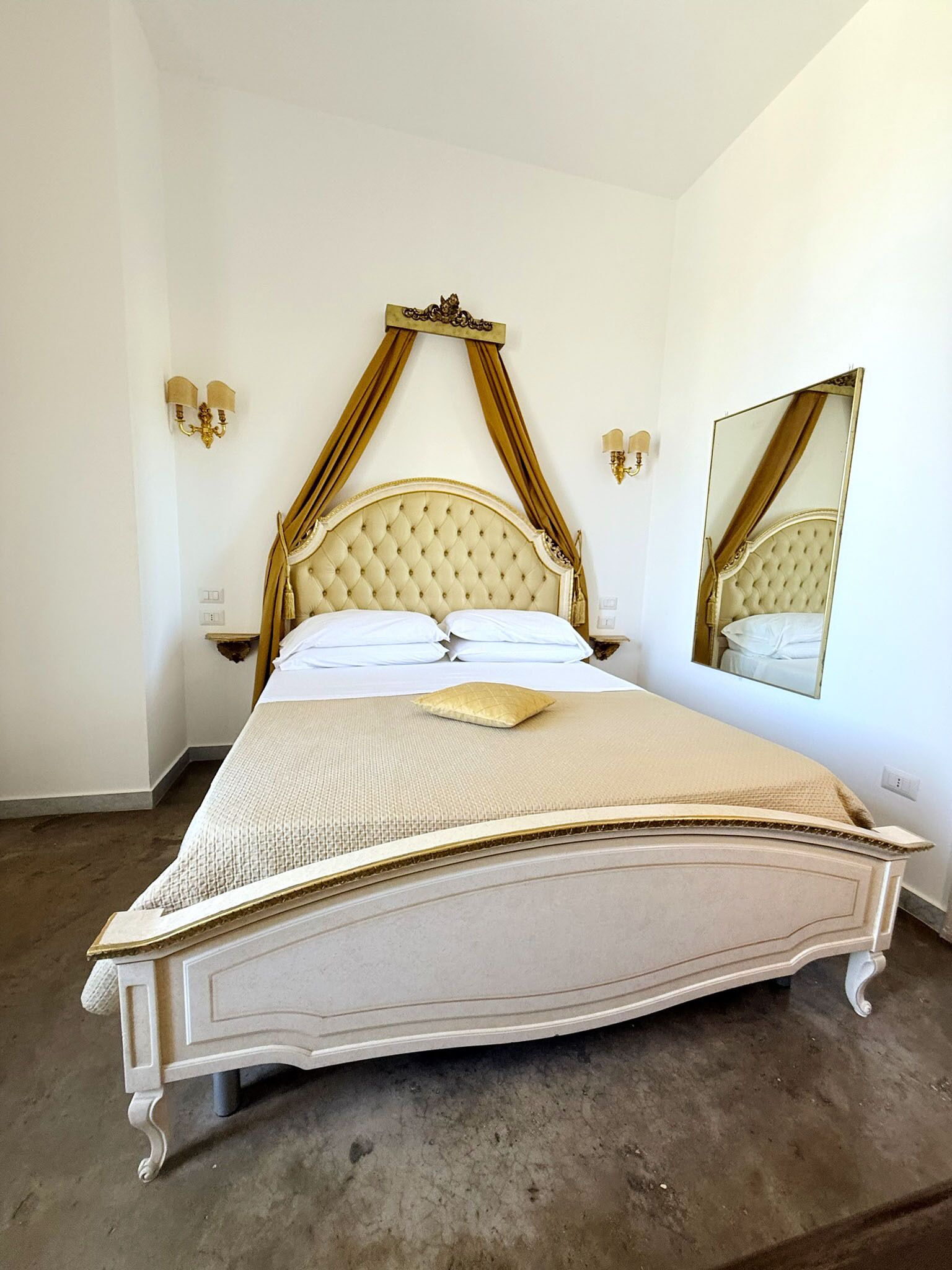 A large bed with a tufted headboard, a canopy, and a mirror on the wall.
