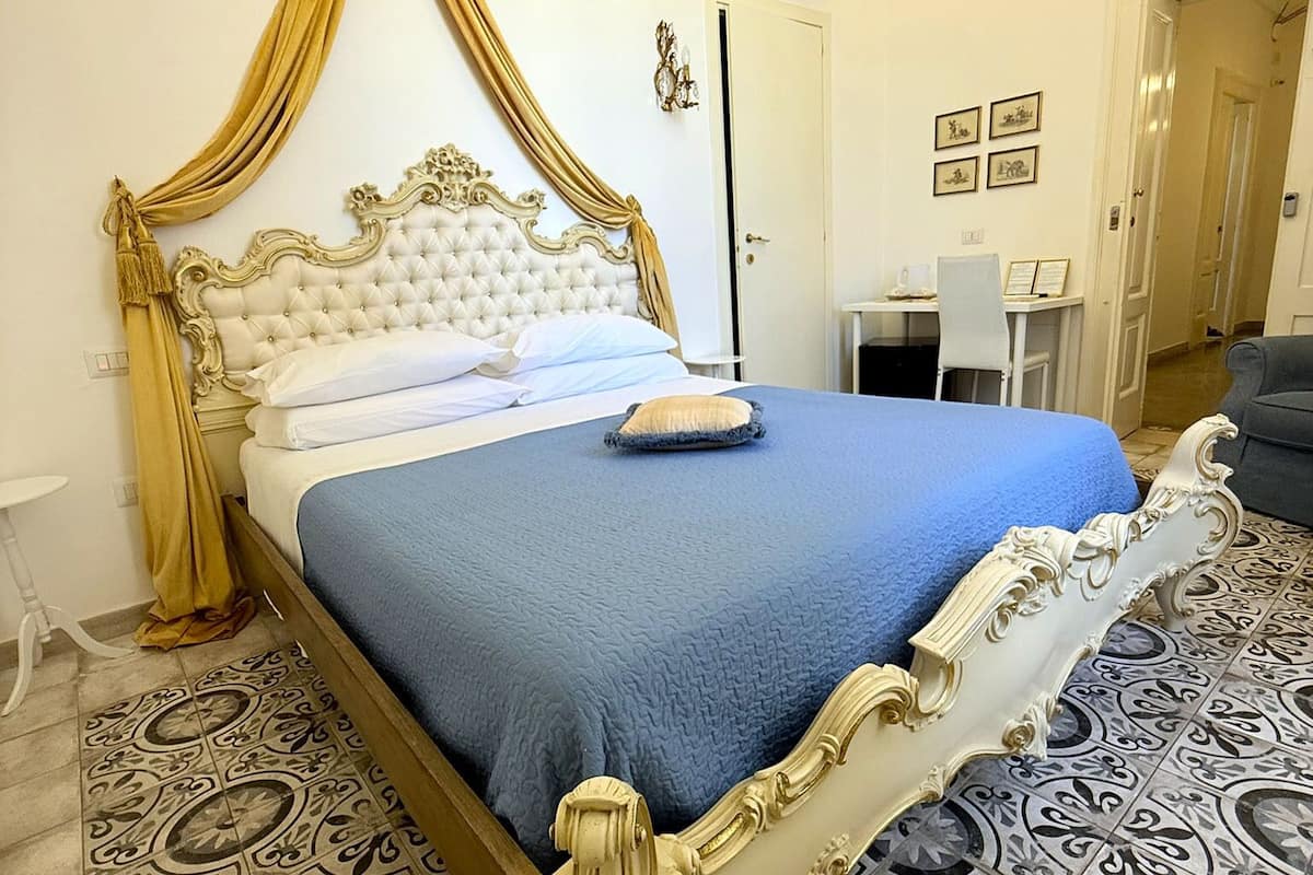 Un lit doté d’une tête de lit blanche et dorée, richement décorée, d’une couvre-lit bleue et d’un rideau doré.