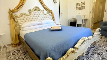 Uma cama com cabeceira branca e dourada ricamente decorada, colcha azul e cortina dourada.