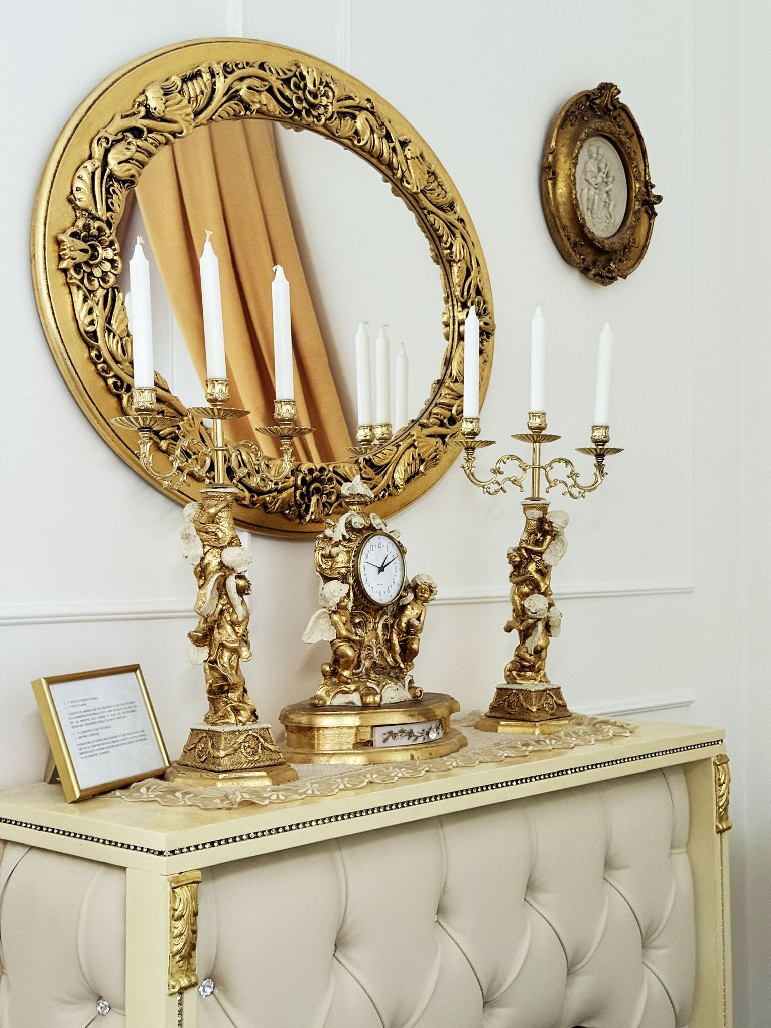 Uma luxuosa mesinha de banho com um espelho emoldurado a ouro, castiçais elaborados e um relógio.