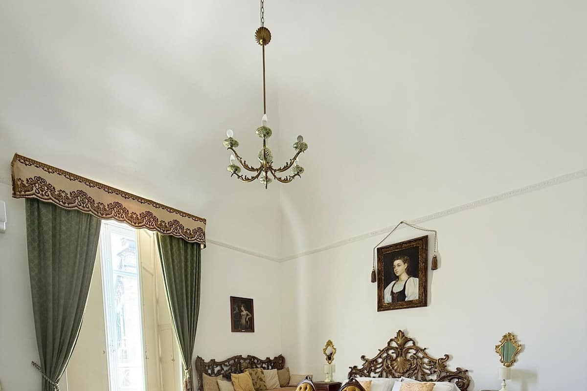 Une chambre avec deux lits, un lustre, un canapé vert et une grande fenêtre avec des rideaux.