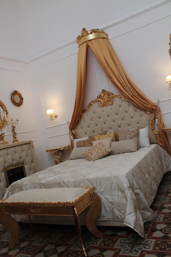 A luxurious bedroom with a tufted headboard, a canopy bed, a matching footboard, and a bedside table with a lamp.