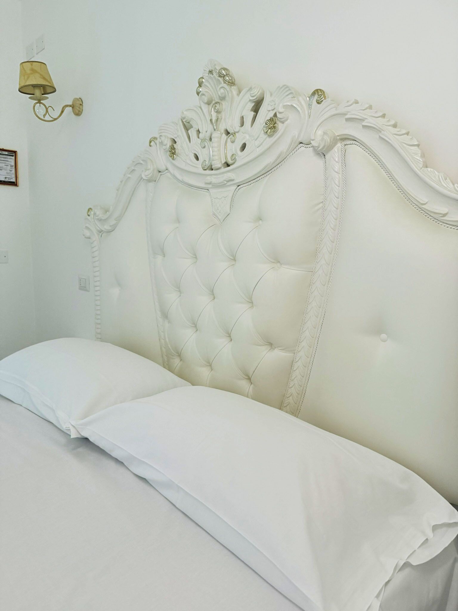 Una cama con cabecera capitonada y un único cojín blanco.