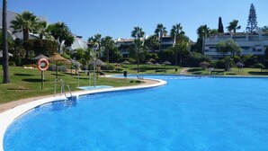 A large swimming pool with a curved edge, surrounded by palm trees and a clear blue sky. - Duplex Penthouse Lunamar (Marbella)