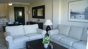A living room with two white sofas, a coffee table with a plant, a lamp, and a framed picture on the wall. - Duplex Penthouse Lunamar (Marbella)