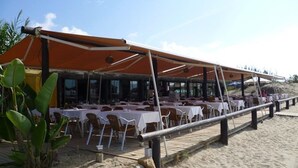 An outdoor restaurant with tables and chairs under a large canopy, overlooking a sandy beach. - Duplex Penthouse Lunamar (Marbella)