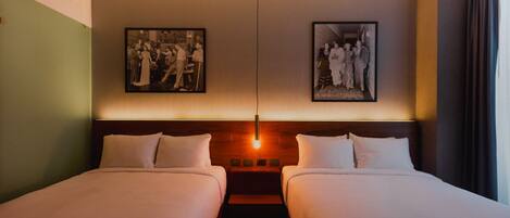 A hotel room with two beds, a headboard with a light fixture, and two framed photographs on the wall.