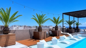 Una piscina en la azotea con sillas de descanso, palmeras y vistas del horizonte de la ciudad.