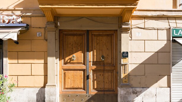 A double wooden door with a metal kick plate, a small sign above the door, and a street sign to the right. - Dolce Luxury Rooms (Rome)