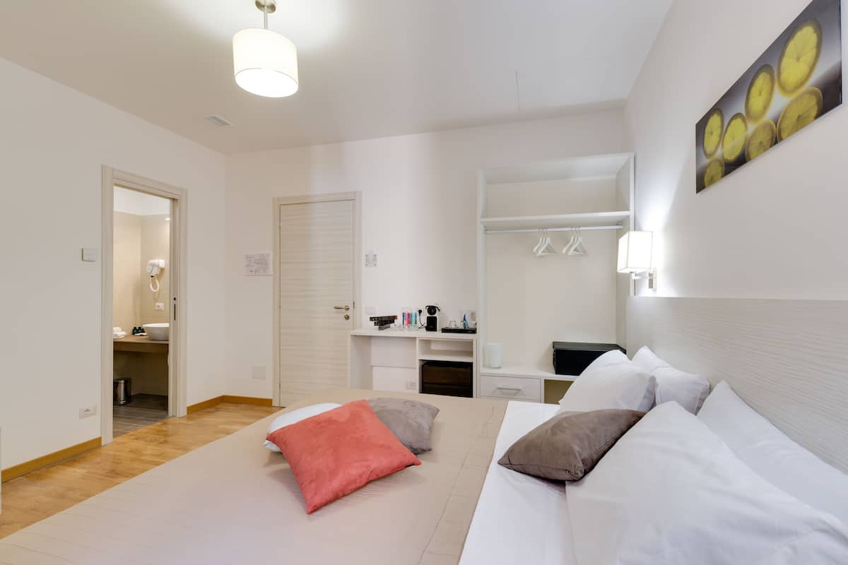 A hotel room with a bed, pillows, a desk, a chair, a mirror, and a wardrobe.