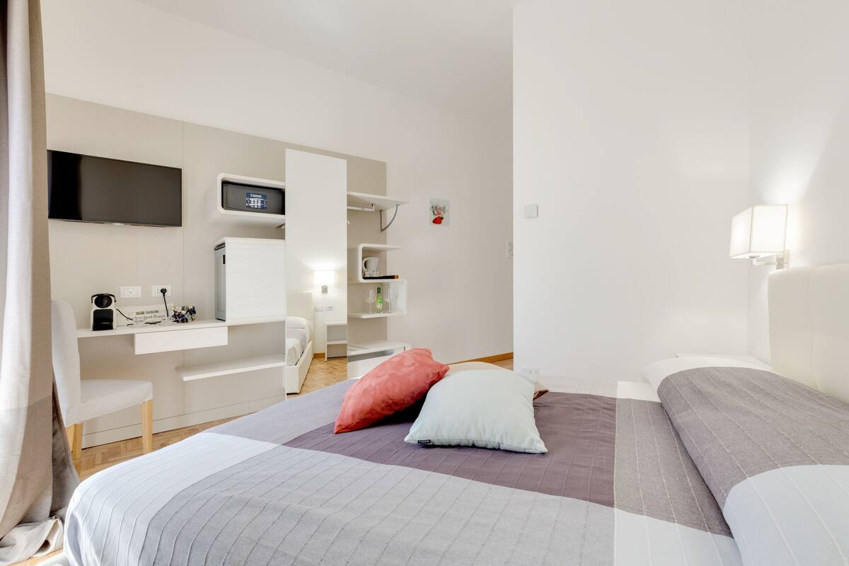 A modern hotel room with a large bed, a desk with a computer, a flat-screen TV, and a small seating area.