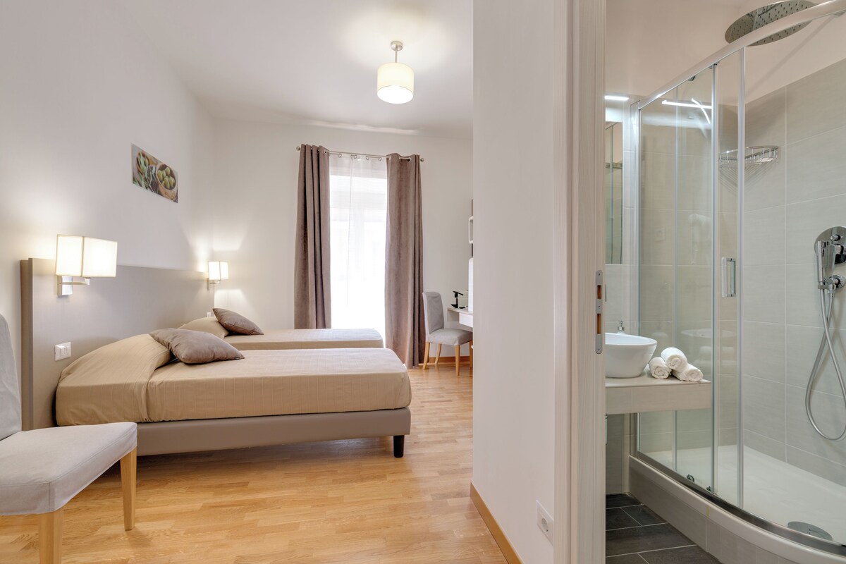 A modern hotel room with two beds, a shower, and a desk with a chair.