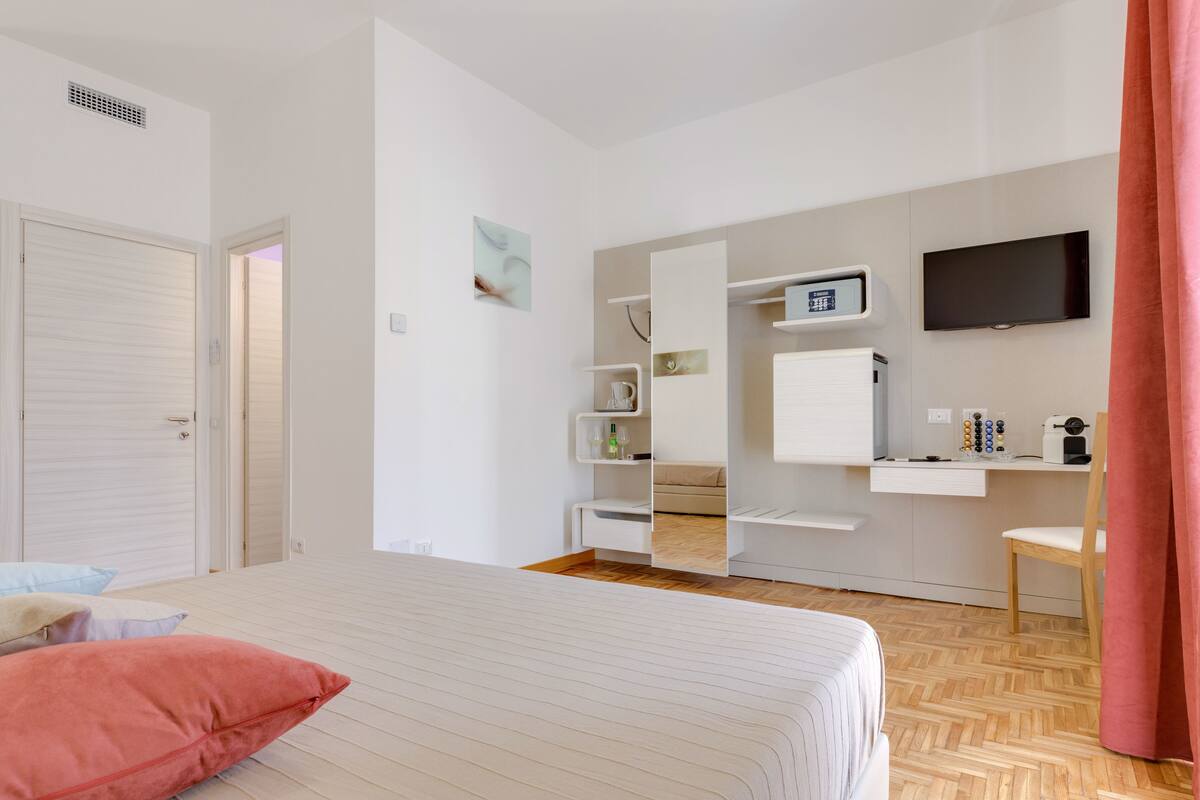 A hotel room with a bed, a desk with a computer, a TV, and a wardrobe.