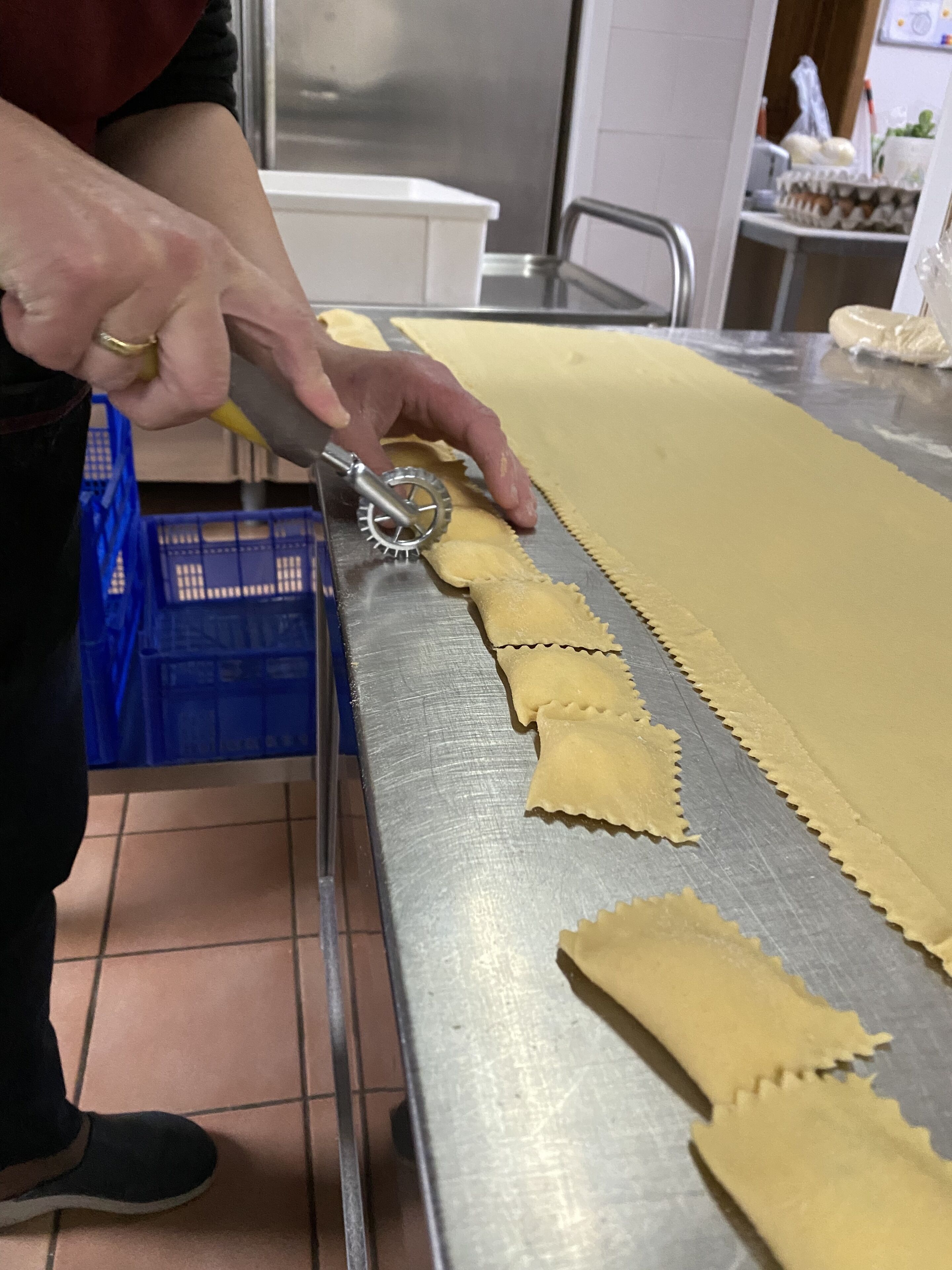 Una persona usando un cortador de pasta sobre una lámina larga de masa.