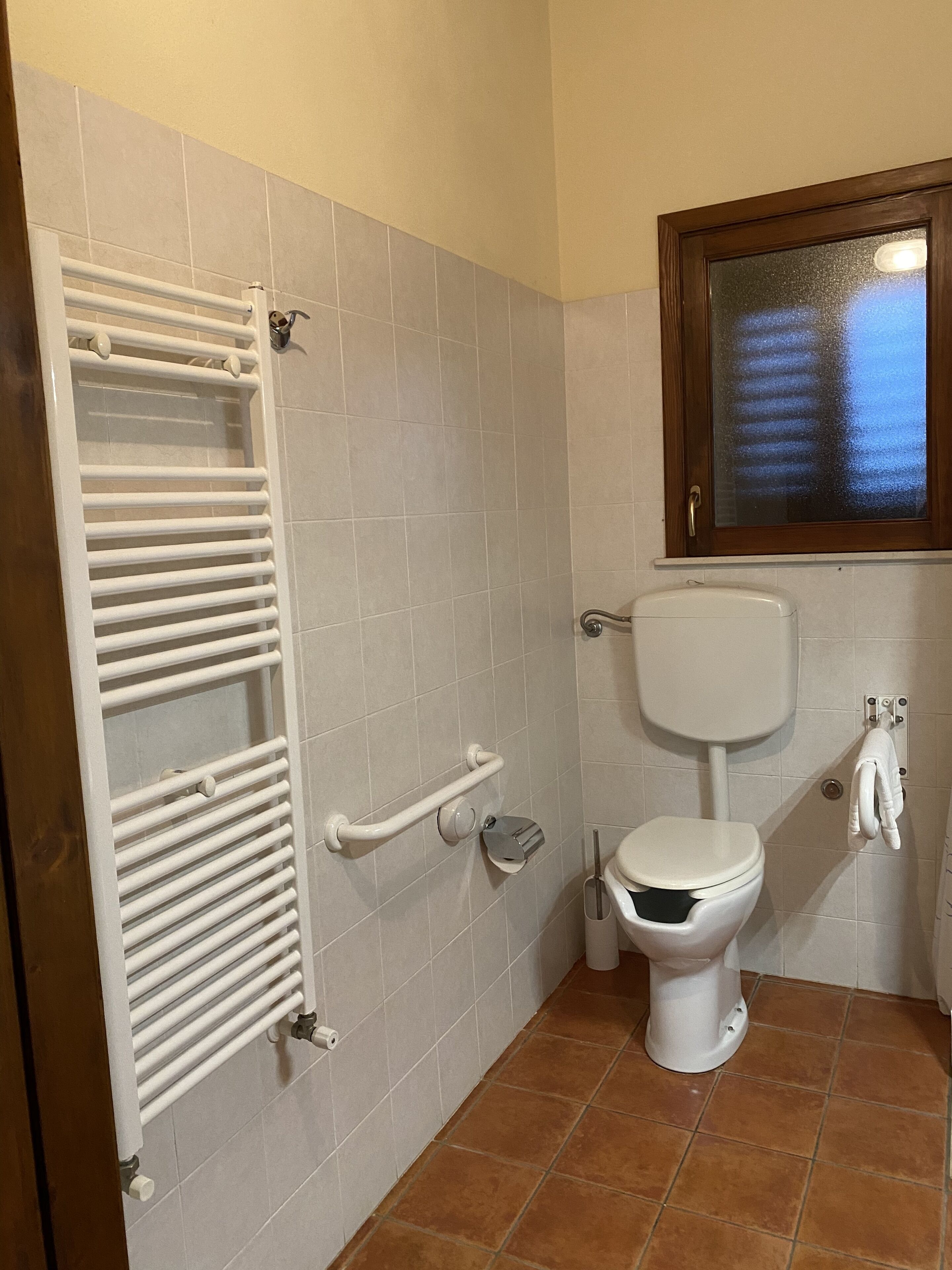 A bathroom with a white toilet, a white towel rack, and a hand dryer.