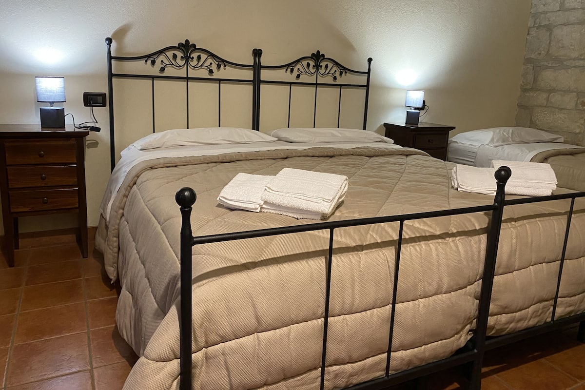 A neatly made bed with a beige quilt, two bedside tables with lamps, and a stone wall.