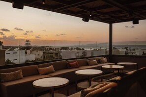 Una terraza en la azotea con un sofá, mesas redondas y vistas panorámicas de la ciudad.