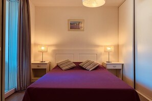 A hotel room with a large bed, two bedside tables with lamps, a picture on the wall, and a window with curtains.