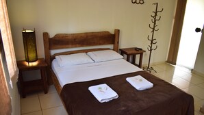 Un lit bien fait, recouvert d’une couverture marron, avec deux oreillers et deux serviettes pliées posées dessus. On aperçoit une table de chevet avec une lampe, ainsi qu’une petite table placée à côté du lit.
