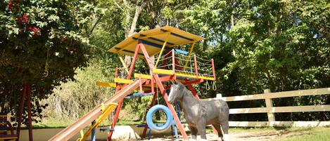 A playground with a slide, climbing structure, and a horse statue.