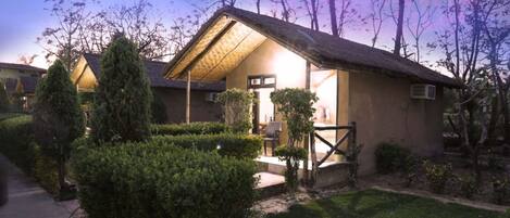 A single-story building with a thatched roof, surrounded by well-maintained hedges and trees.