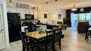 A modern kitchen with white cabinets, a black refrigerator, and a dining area with a wooden table and chairs. - Lake Vacation Condo A-5 on Table Rock Lake by RedAwning (Hollister)