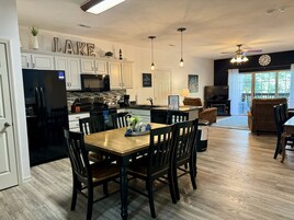 Una cocina moderna con armarios blancos, un refrigerador negro y un comedor con mesa y sillas de madera.
