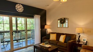 A living room with a sofa, coffee table, and lamps. There is a large window with curtains, a clock on the wall, and a view of the outdoors. - Lake Vacation Condo A-5 on Table Rock Lake by RedAwning (Hollister)