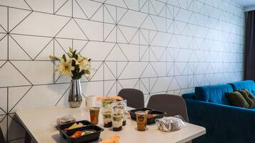 Een eettafel met maaltijdverpakkingen, een vaas met bloemen en een blauwe bank op de achtergrond.