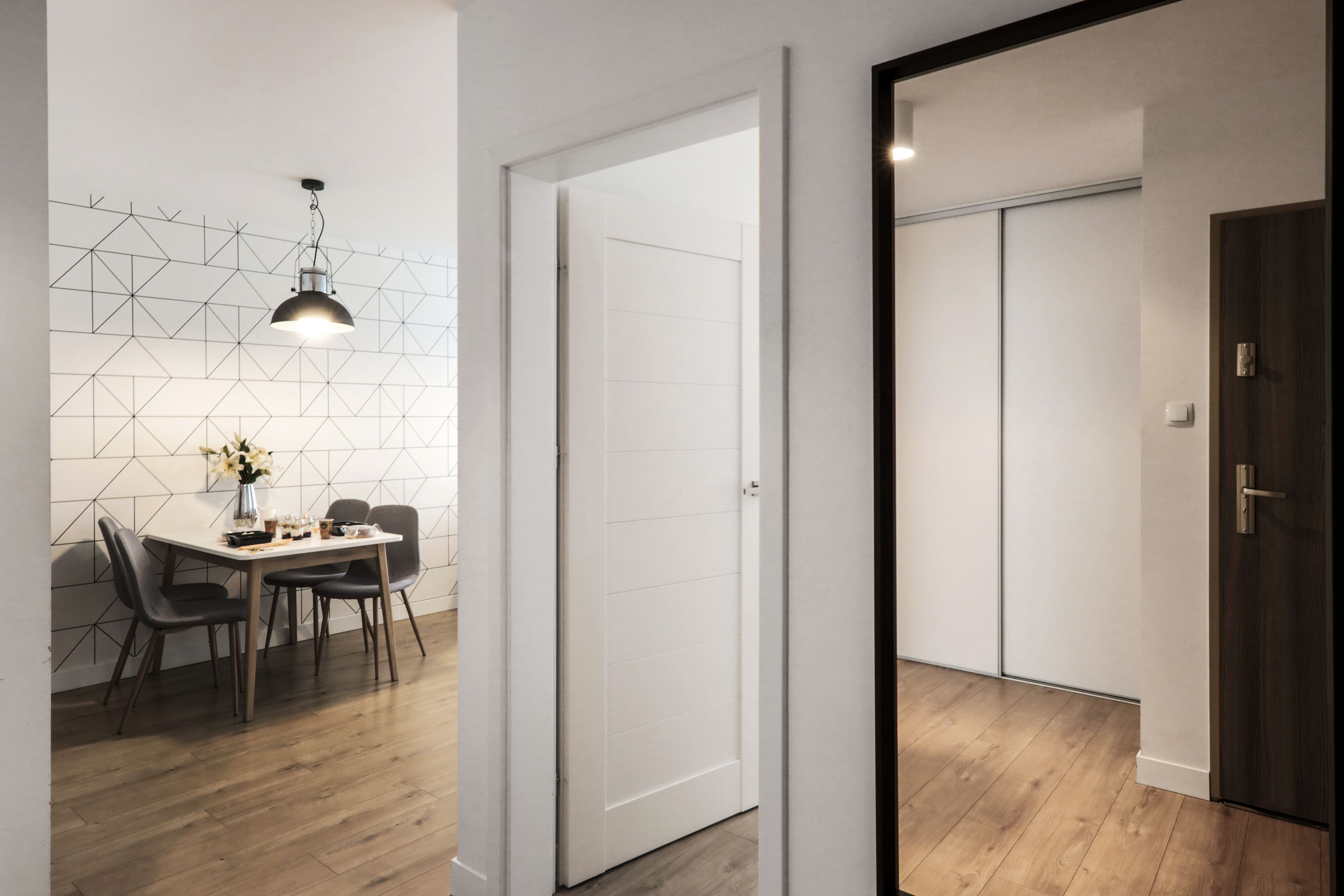 Un interior moderno con comedor, una puerta blanca y piso de madera.