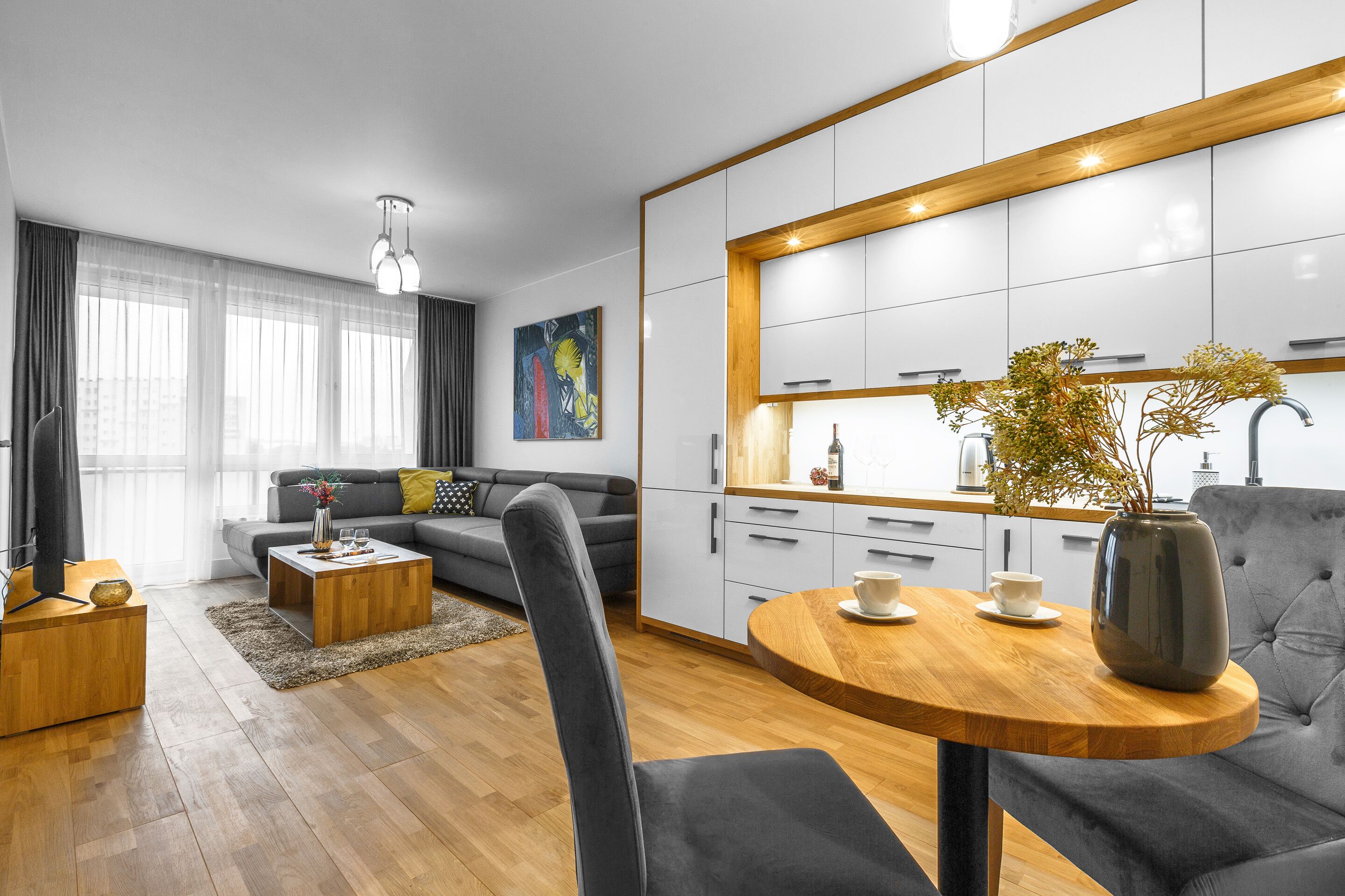 Een moderne woonkamer met een bank, salontafel en een eethoek met een vaas en kopje.