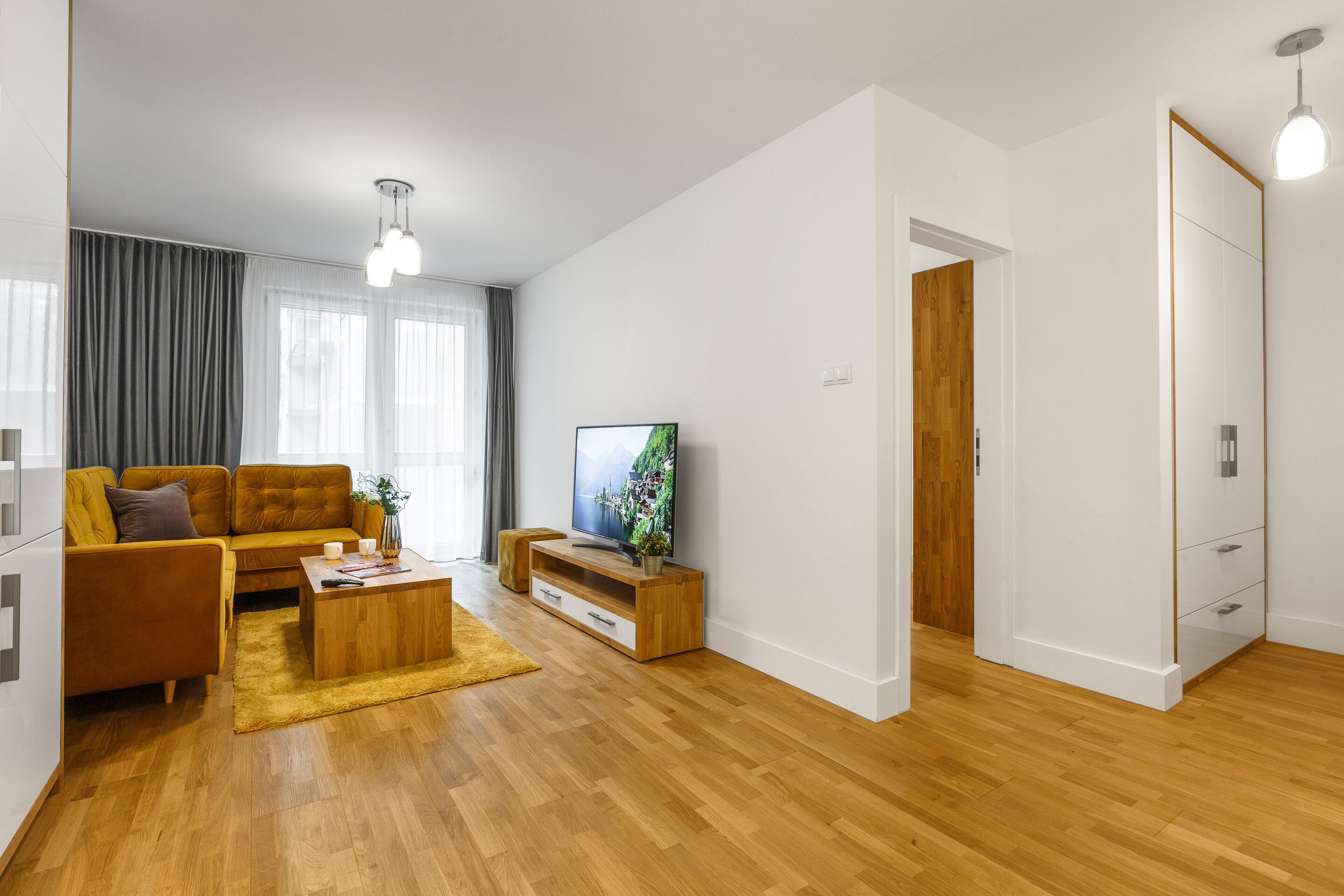 A modern living room with a sofa, coffee table, TV, and wooden flooring.