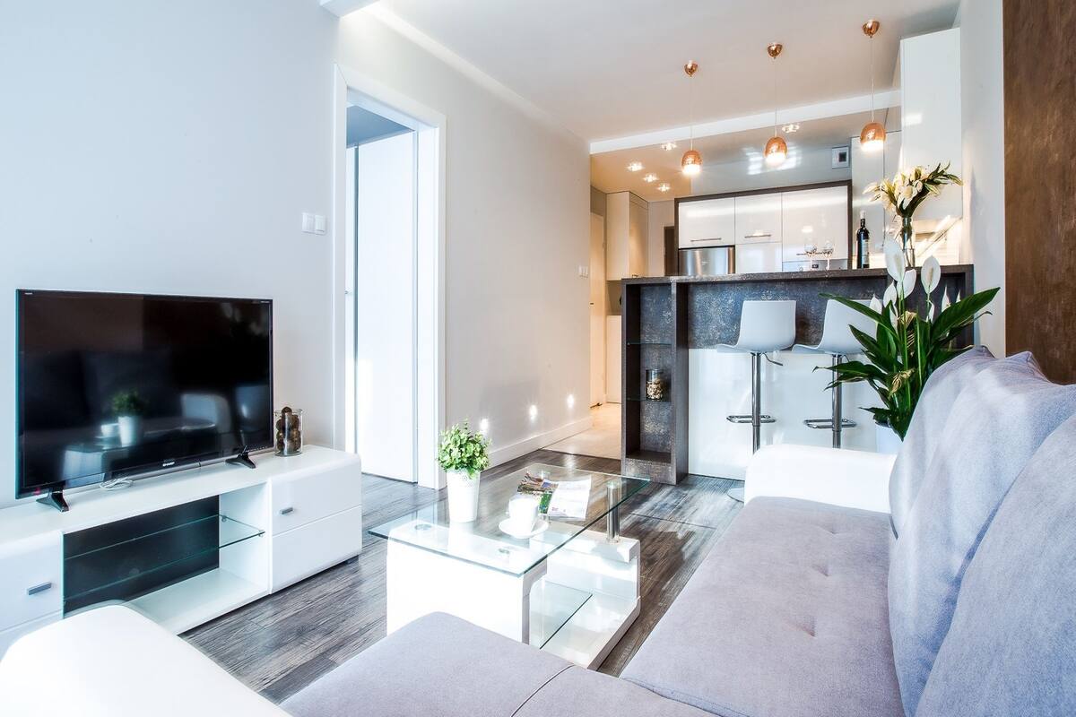 A modern living room with a flat-screen TV, a glass coffee table, and a grey sofa.