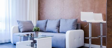 Una sala de estar moderna con un sofá gris, una mesa de centro de vidrio y dos taburetes blancos.