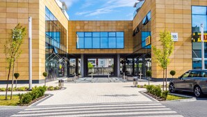 A modern building with a central entrance, glass facade, and a car parked in front. - Emihouse CityVibe Apartments (Rzeszów)