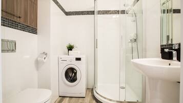 Ein modernes Badezimmer mit Waschmaschine, Toilette, Duschkabine und Waschbecken.