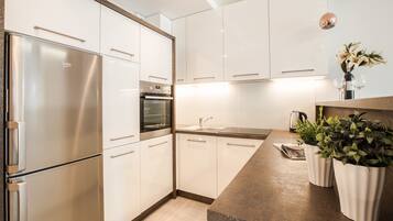A modern kitchen with white cabinets, a stainless steel refrigerator, an oven, and a granite countertop.